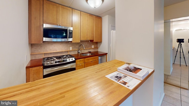 kitchen with tasteful backsplash, butcher block counters, sink, and appliances with stainless steel finishes