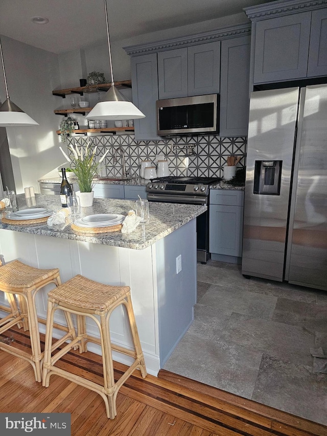 kitchen featuring light stone countertops, stainless steel appliances, a breakfast bar area, decorative backsplash, and hardwood / wood-style flooring