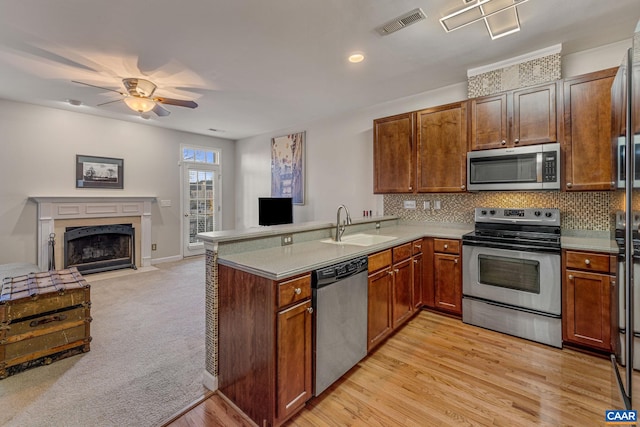 kitchen with kitchen peninsula, backsplash, stainless steel appliances, sink, and light hardwood / wood-style flooring