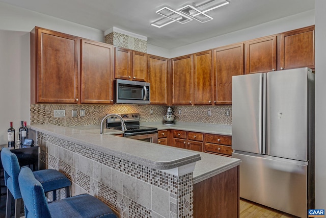 kitchen featuring kitchen peninsula, appliances with stainless steel finishes, light wood-type flooring, and a kitchen bar