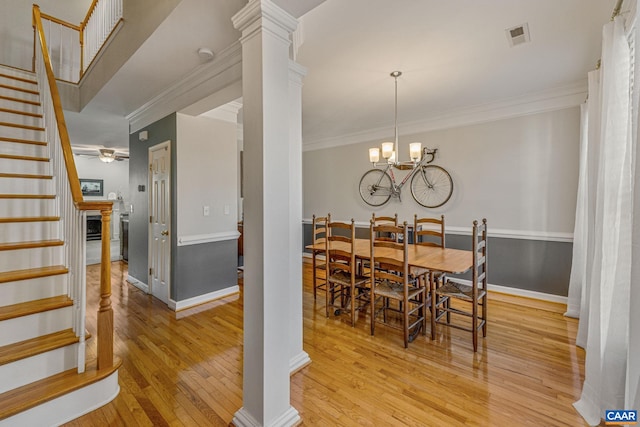 dining space featuring ornate columns, crown molding, ceiling fan with notable chandelier, and light wood-type flooring