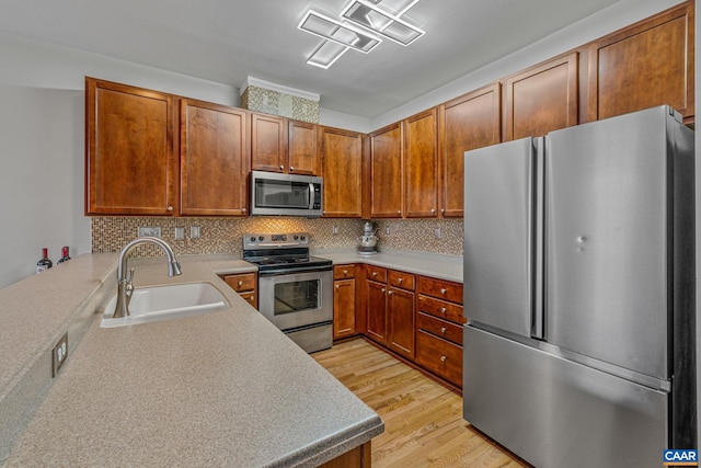 kitchen with kitchen peninsula, appliances with stainless steel finishes, light wood-type flooring, tasteful backsplash, and sink