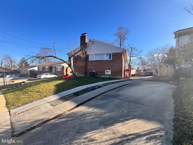 view of side of home featuring a yard, brick siding, central AC, and a chimney