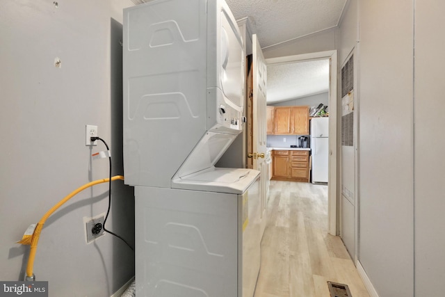 washroom featuring stacked washing maching and dryer, a textured ceiling, and light hardwood / wood-style floors