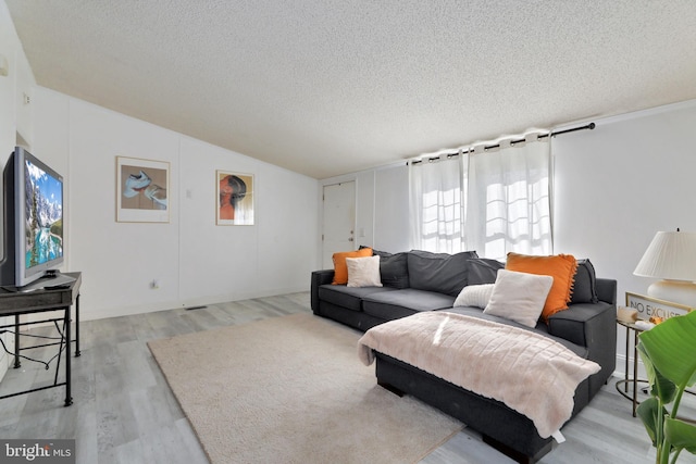 living room featuring a textured ceiling, light hardwood / wood-style floors, and vaulted ceiling