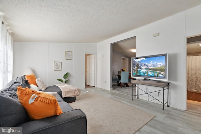 living room with a textured ceiling, vaulted ceiling, and light wood-type flooring