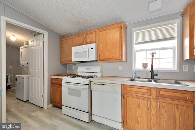 kitchen featuring sink, stacked washing maching and dryer, light hardwood / wood-style floors, a textured ceiling, and white appliances