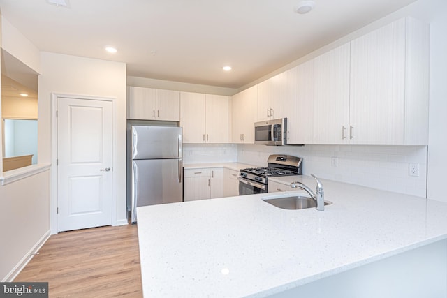 kitchen featuring kitchen peninsula, appliances with stainless steel finishes, light wood-type flooring, light stone countertops, and sink