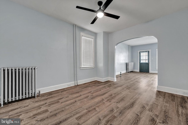 empty room with hardwood / wood-style flooring, ceiling fan, and radiator heating unit