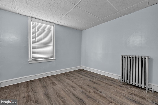 empty room with radiator heating unit, dark hardwood / wood-style flooring, and a paneled ceiling