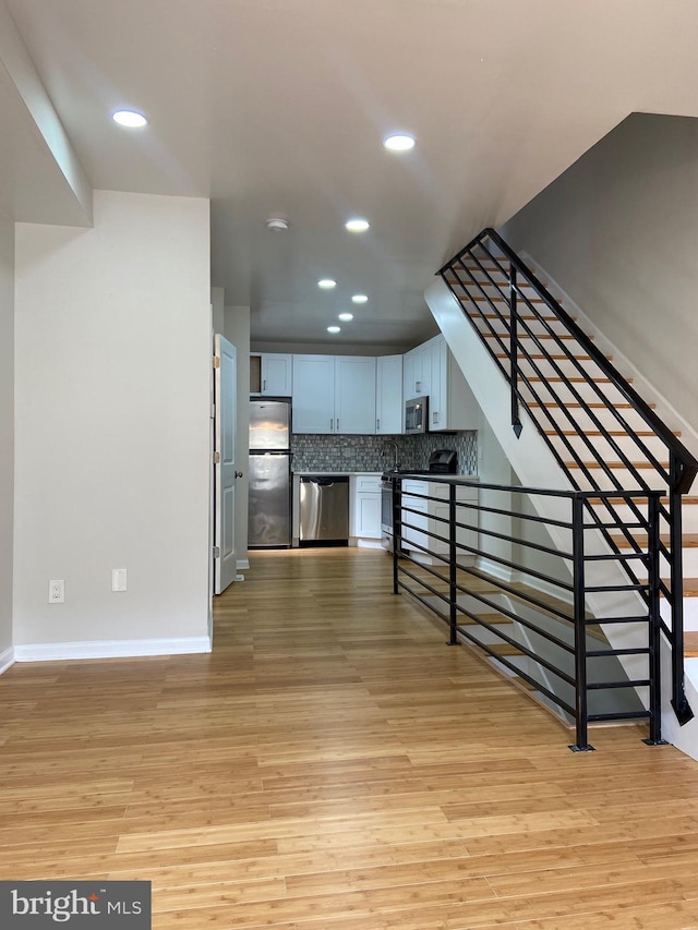 kitchen with decorative backsplash, white cabinets, light hardwood / wood-style floors, and appliances with stainless steel finishes