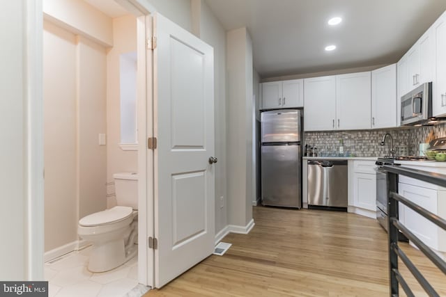 kitchen featuring decorative backsplash, appliances with stainless steel finishes, light hardwood / wood-style flooring, and white cabinetry