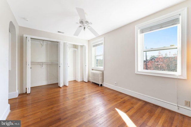 unfurnished bedroom with multiple windows, hardwood / wood-style floors, radiator, and ceiling fan