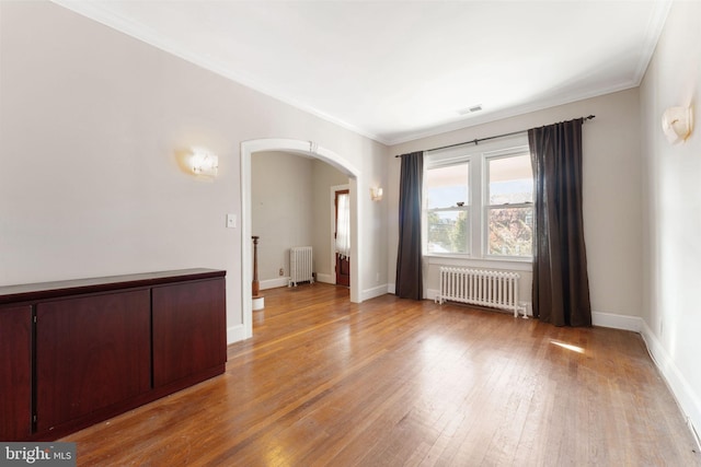 spare room with radiator heating unit, ornamental molding, and light hardwood / wood-style flooring