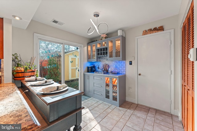 kitchen featuring backsplash, gray cabinets, pendant lighting, and an inviting chandelier