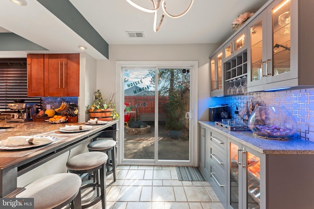 kitchen with backsplash, gray cabinets, light stone countertops, and light tile patterned floors