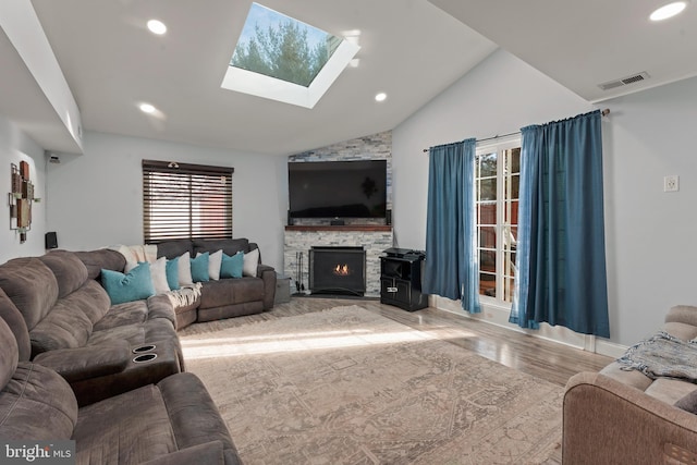 living room featuring a stone fireplace, lofted ceiling with skylight, and wood-type flooring