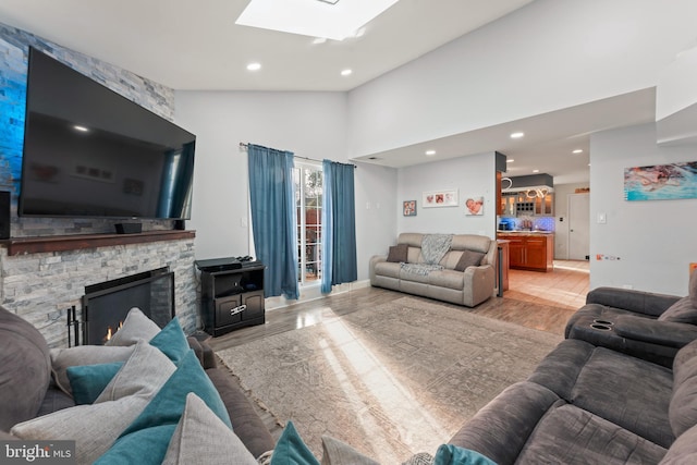 living room featuring a skylight, a fireplace, high vaulted ceiling, and light hardwood / wood-style flooring