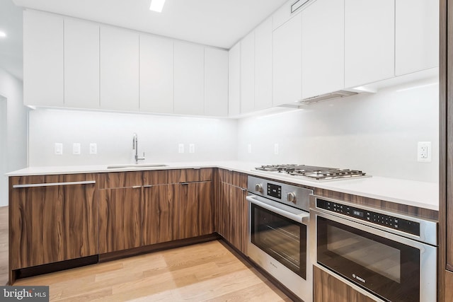 kitchen with light hardwood / wood-style flooring, stainless steel appliances, white cabinetry, and sink