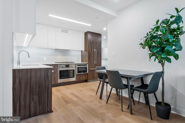 kitchen with appliances with stainless steel finishes, dark brown cabinets, sink, light hardwood / wood-style flooring, and white cabinets