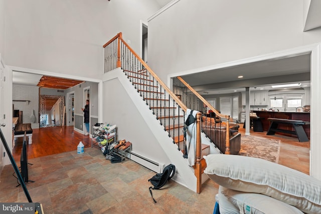 stairway with baseboard heating and a high ceiling