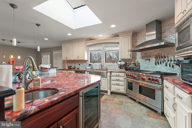 kitchen with wall chimney range hood, wine cooler, a skylight, appliances with stainless steel finishes, and decorative light fixtures