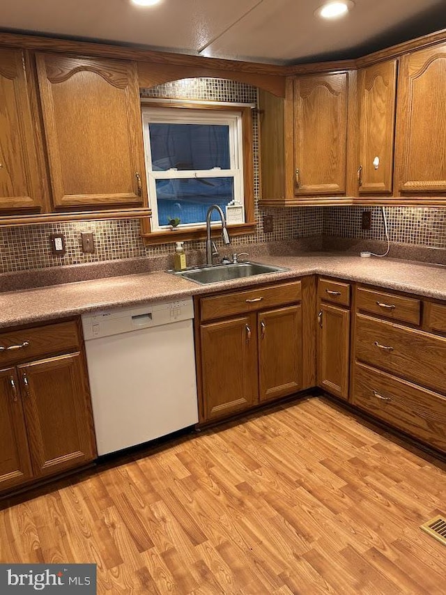 kitchen featuring white dishwasher, decorative backsplash, light wood-type flooring, and sink