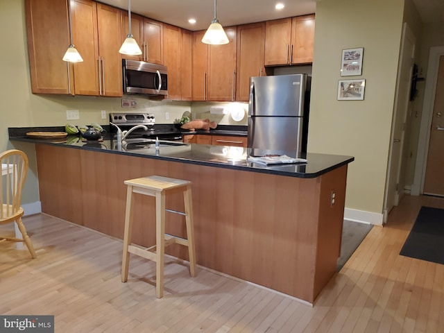 kitchen with light hardwood / wood-style floors, kitchen peninsula, hanging light fixtures, and appliances with stainless steel finishes