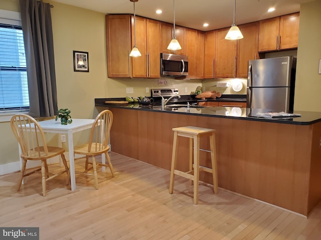 kitchen featuring sink, stainless steel appliances, kitchen peninsula, light hardwood / wood-style floors, and decorative light fixtures