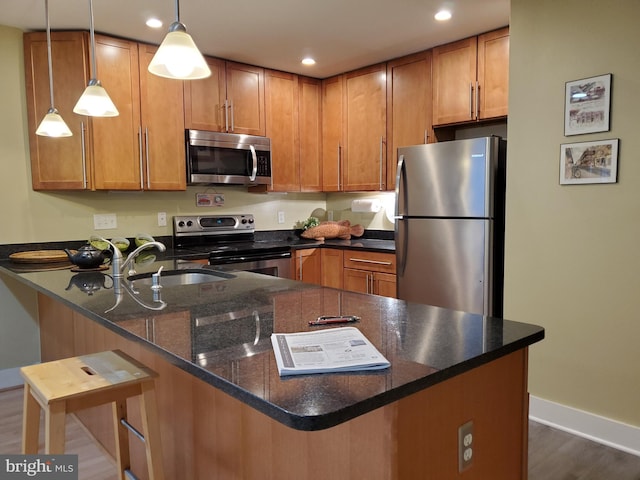 kitchen with a breakfast bar, stainless steel appliances, dark wood-type flooring, sink, and decorative light fixtures