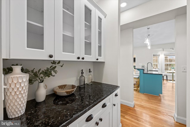 bar with white cabinetry, sink, hanging light fixtures, dark stone countertops, and light hardwood / wood-style floors