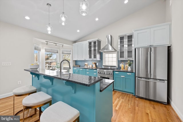 kitchen featuring wall chimney exhaust hood, stainless steel appliances, vaulted ceiling, blue cabinets, and white cabinetry