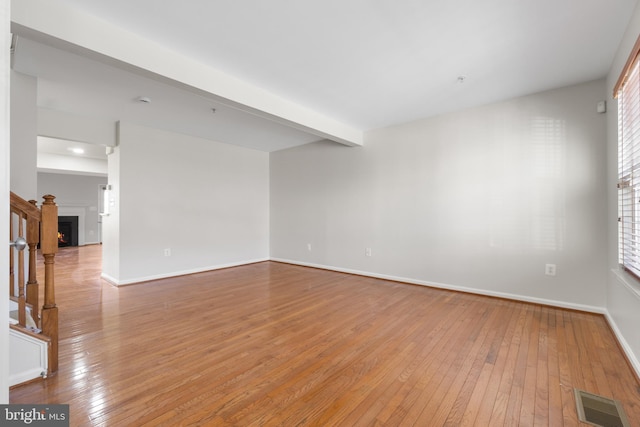 unfurnished room with beam ceiling and light hardwood / wood-style floors