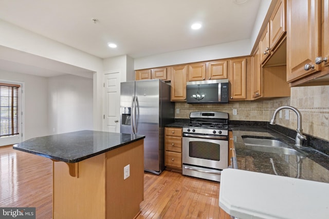 kitchen with appliances with stainless steel finishes, sink, a kitchen bar, decorative backsplash, and light hardwood / wood-style flooring