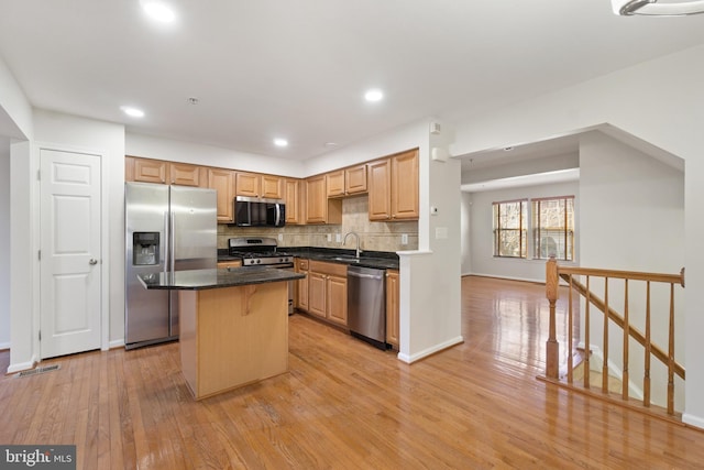 kitchen with sink, light wood-type flooring, a kitchen island, stainless steel appliances, and decorative backsplash