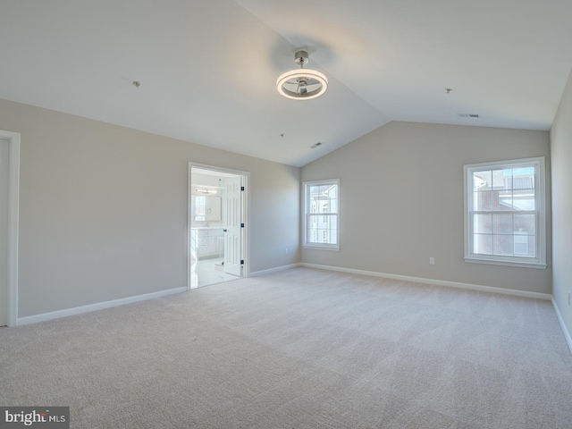 spare room featuring light carpet, a healthy amount of sunlight, and vaulted ceiling