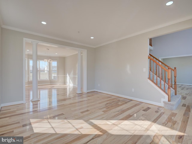 spare room featuring a chandelier, light wood-type flooring, decorative columns, and crown molding