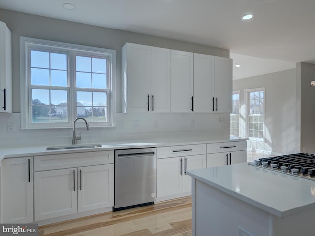 kitchen with sink, light wood-type flooring, tasteful backsplash, white cabinetry, and stainless steel appliances