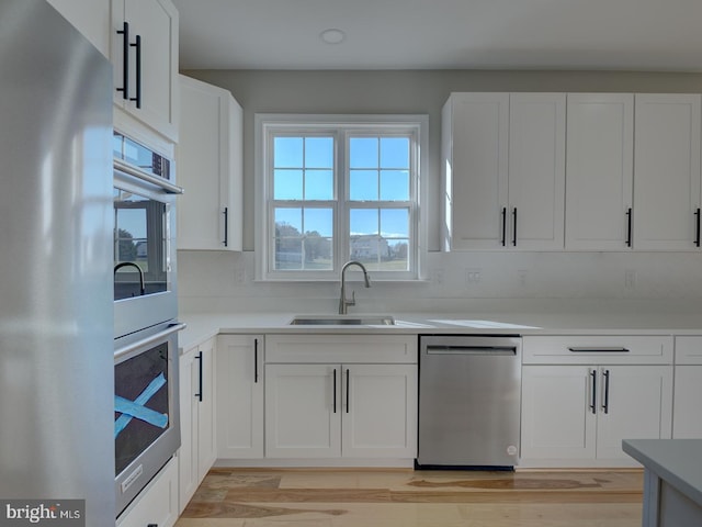 kitchen featuring white cabinetry, sink, stainless steel appliances, tasteful backsplash, and light hardwood / wood-style flooring