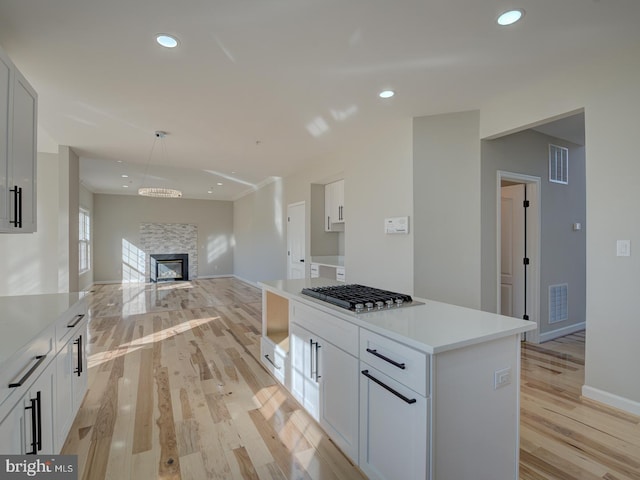 kitchen featuring a fireplace, light hardwood / wood-style flooring, white cabinetry, and stainless steel gas cooktop