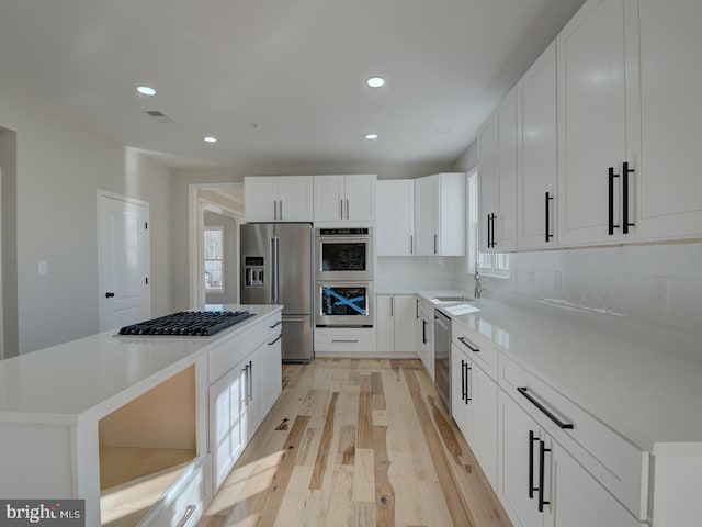 kitchen featuring a center island, sink, appliances with stainless steel finishes, light hardwood / wood-style floors, and white cabinetry