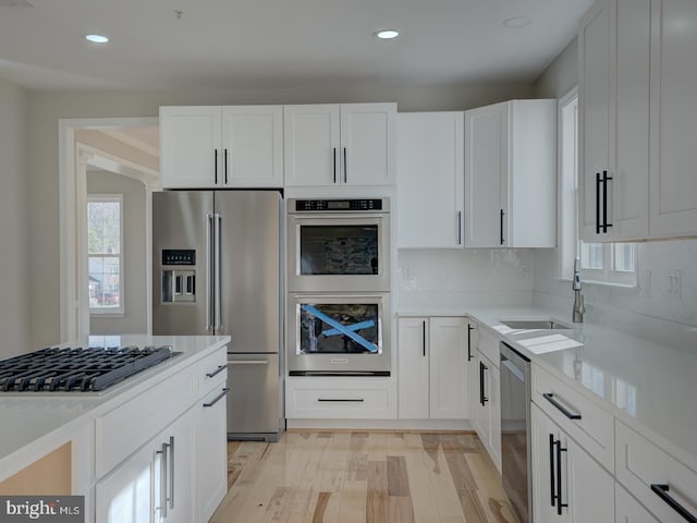 kitchen with white cabinets, backsplash, stainless steel appliances, and light hardwood / wood-style floors