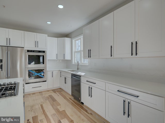 kitchen with white cabinets, sink, decorative backsplash, light wood-type flooring, and appliances with stainless steel finishes