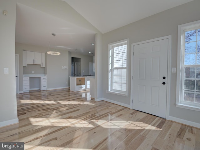 foyer entrance with built in desk, light hardwood / wood-style floors, vaulted ceiling, and a wealth of natural light