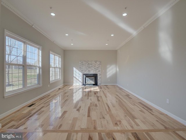 unfurnished living room featuring light hardwood / wood-style floors, a stone fireplace, and crown molding