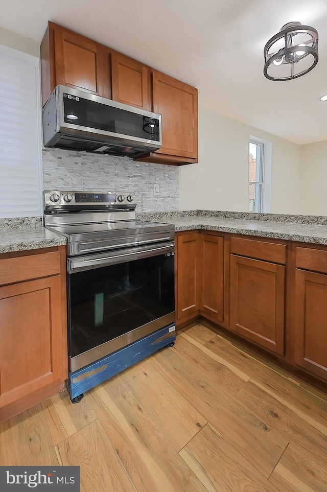 kitchen with light stone counters, backsplash, appliances with stainless steel finishes, and light hardwood / wood-style flooring