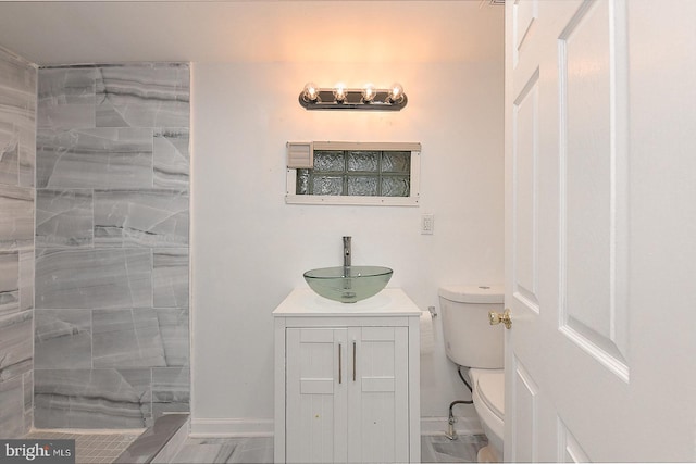 bathroom with a tile shower, vanity, and toilet