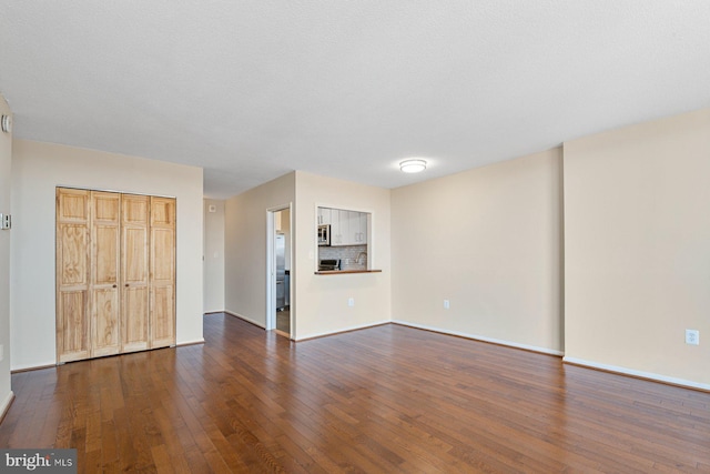 unfurnished living room featuring baseboards and dark wood-type flooring