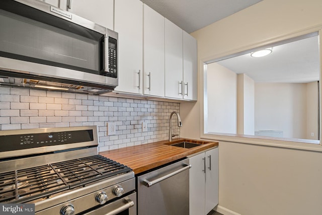 kitchen featuring a sink, wood counters, tasteful backsplash, stainless steel appliances, and white cabinets