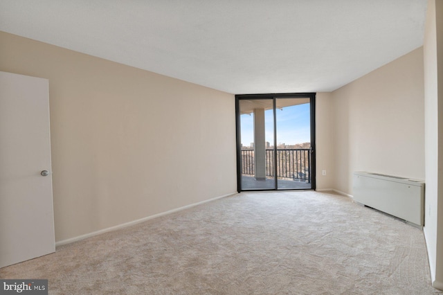 empty room featuring expansive windows, baseboards, carpet flooring, and radiator heating unit